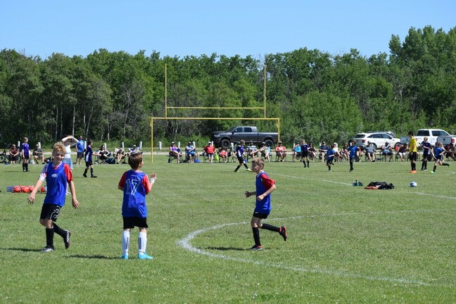 Children playing soccer on the soccer field with spectators.