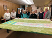 Group of quilters around a large quilt.