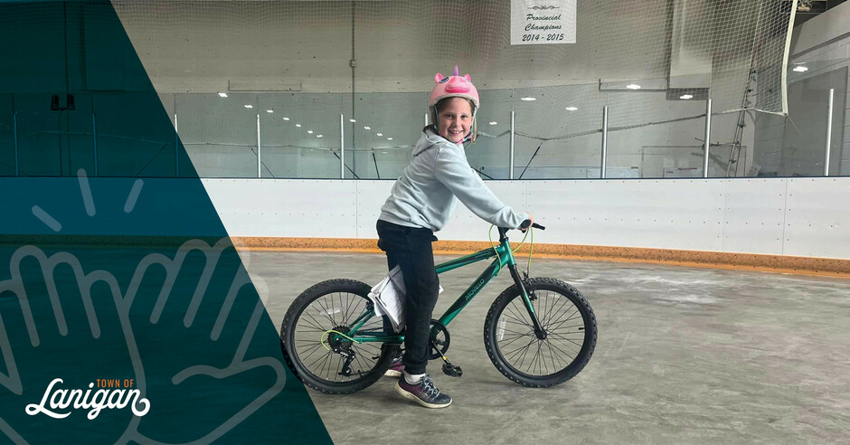 Smiling child on bike at the Lanigan Recreation Complex arena. 